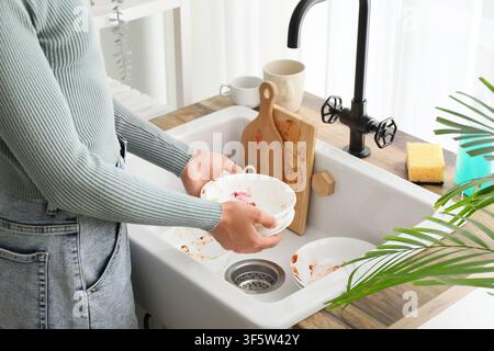 Womans hands holding dirty dishes over a kitchen sink with cutting boards and a sponge, household chores Stock Photo