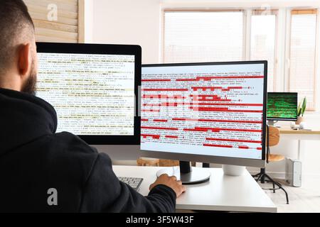 Back view of a male programmer coding on multiple computer screens in a modern office environment, the screens display lines of code, the technical na Stock Photo