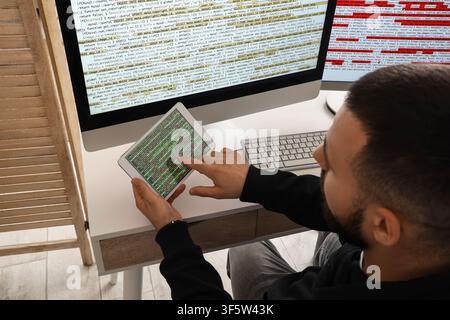 Programmer working on a tablet and desktop computer with code on screen, software development and cybersecurity Stock Photo
