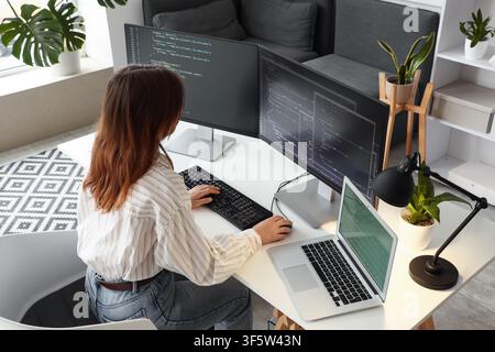 Female software developer coding on multiple computer screens and laptop in a modern home office environment, the modern home office environment suppo Stock Photo