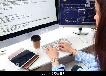 Female programmer coding on a desktop computer with multiple screens displaying complex software development code, the womans hands are actively typin Stock Photo