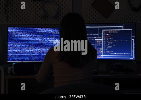 Female programmer working on computer code at night, cybersecurity and software development concept, dark room environment Stock Photo