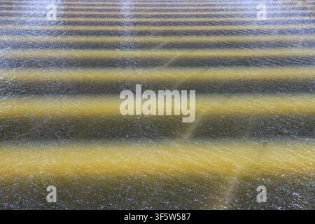 A close-up view of water surface featuring alternating golden and dark horizontal ripples, with delicate water particles and subtle textures, creating Stock Photo