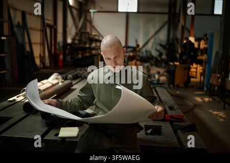 Male Welder Examining Blueprint in Industrial Metal Workshop Stock Photo