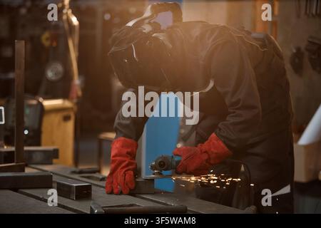 Male Welder in Protective Gear Grinding Metal in Workshop Stock Photo