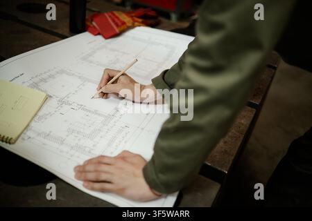Male Welder Drawing on Blueprint Plan in Metal Workshop Stock Photo