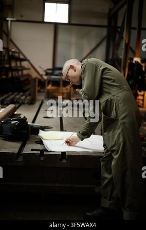 Male Welder Examining Blueprint in Metal Workshop Stock Photo