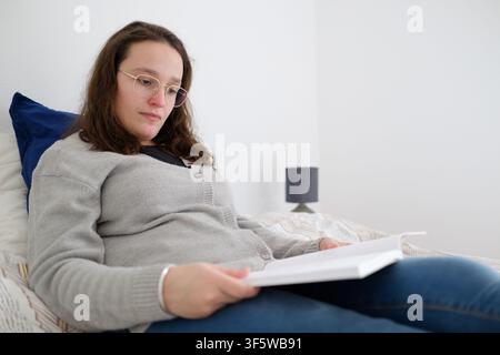 Young woman relaxing and enjoying reading a book in her bed at home Stock Photo