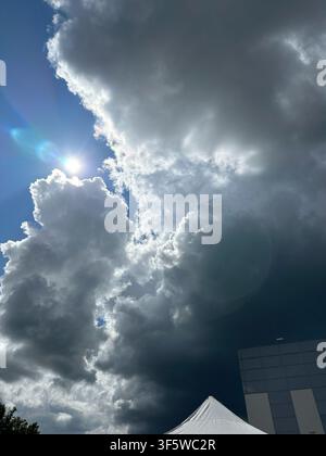 Towering dark storm clouds illuminated by sunlight above an urban setting, creating a striking contrast between light and shadow. Ideal for weather, c Stock Photo