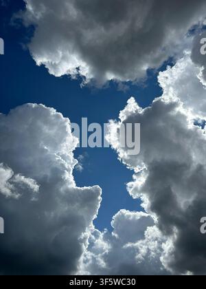 Towering cumulus storm clouds surround a vivid blue sky, creating a dramatic natural frame with striking light and shadow. Perfect for weather, climat Stock Photo