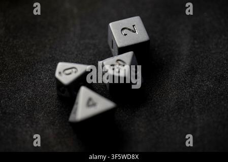 Strategic board game concept featuring dark metal multi sided dice scattered on dark fabric Stock Photo