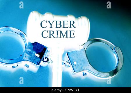 Close-up futuristic concept image of a judge's gavel and metallic handcuffs featuring the words "Cyber Crime". The scene is presented on a deep blue d Stock Photo