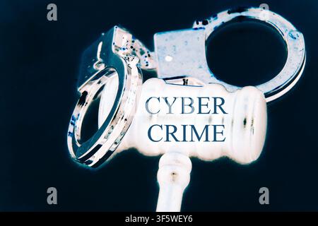 Close-up conceptual image of a judge's gavel and metallic handcuffs featuring the words "Cyber Crime". The scene is set against a deep black backgroun Stock Photo