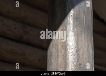 Sunlight falls across a hand-hewn wooden post inside a rustic cabin, accentuating grain, knots and varnished texture. Warm natural tones and shadow cr Stock Photo