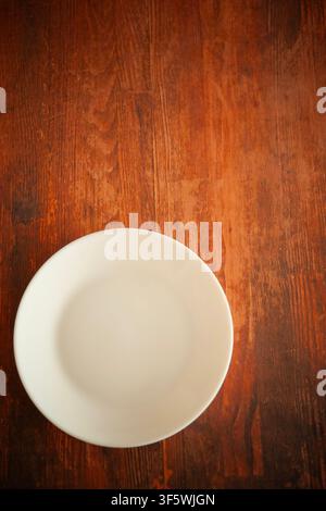 Empty white ceramic plate on a rustic wooden table, photographed from above off center, with ample copy space Stock Photo