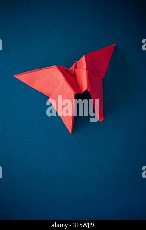 Red origami butterfly on a dark blue background, photographed from above with broad copy space and soft dramatic lighting Stock Photo