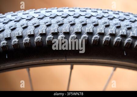 Close-up view of textured knobby tread pattern on black mountain bike tire mounted on wheel rim against soft warm background, showcasing details for c Stock Photo