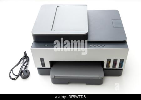 A modern multifunction inkjet printer with visible ink tanks and a power cord sits on a plain white surface Stock Photo