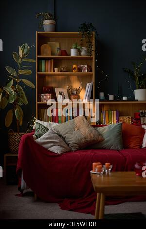 Cozy living room interior featuring wooden bookshelf and red sofa with pillows. Perfect for home decor marketing, interior design inspiration, and lifestyle blogs, vertical Stock Photo
