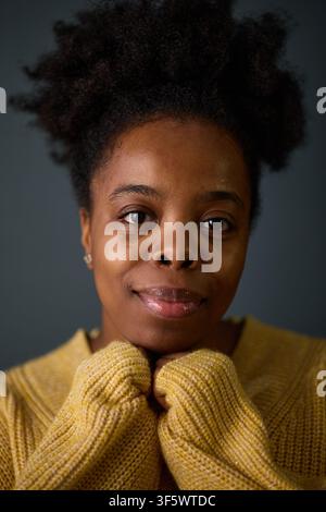 Portrait of young adult African American woman smiling with hands under chin, representing mental wellbeing and self care. Ideal for healthcare and lifestyle marketing, vertical Stock Photo