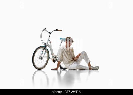 Young cyclist sits beside bicycle and checks smartphone on floor Stock Photo