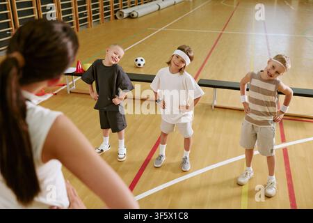 Female Trainer Teaching Children Stretching Exercises in Gym Stock Photo