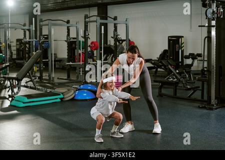 Woman Instructor Guiding Child Doing Squat Exercises in Gym Stock Photo