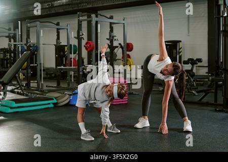 Female Trainer and Child Doing Side Bend Stretch in Gym Stock Photo
