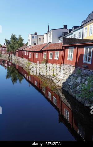Traditional red wooden houses reflected in river water along stone wall Stock Photo
