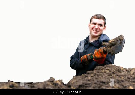 Smiling male worker wearing gloves and holding a shovel while digging soil, isolated on white background, manual labor and construction concept. Stock Photo