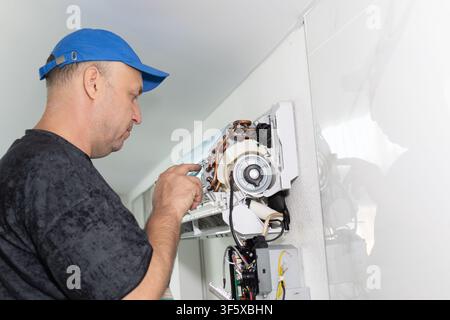 Technician repairing indoor air conditioner unit. Professional maintenance service in bright daylight Stock Photo