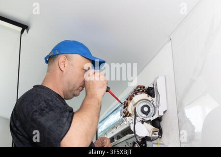 Technician fixing indoor air conditioner unit with screwdriver. Repair service for cooling system home Stock Photo