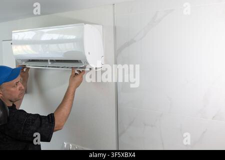 Technician repairing air conditioner on wall. Professional worker fixing climate control system unit Stock Photo