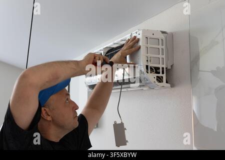 Repairman fixing wall air conditioner with screwdriver. Maintenance and professional service of climate system Stock Photo
