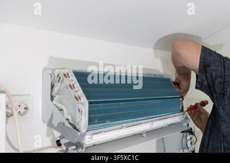 Technician repairing air conditioner on wall. Professional worker fixing cooling system. HVAC maintenance Stock Photo