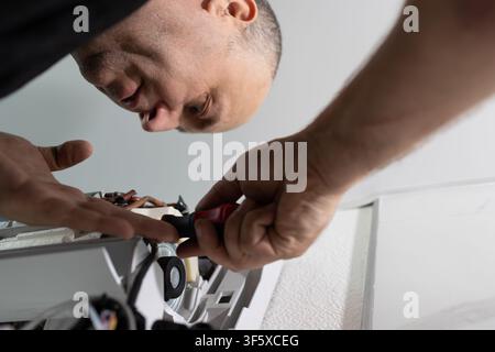 Repairman fixing indoor air conditioner unit with screwdriver. Professional HVAC technician at work Stock Photo