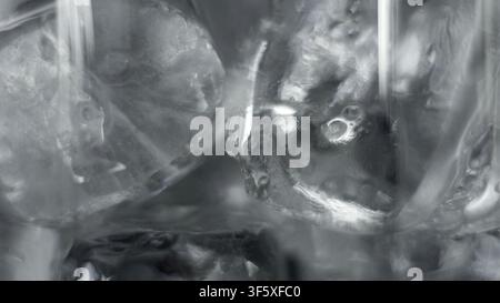 Ice cubes melt in clear water, bubbles rise, creating a cool, abstract texture Stock Photo