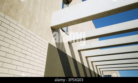 Modern building facade with strong geometric concrete beams creating abstract shadows under a bright blue sky Stock Photo