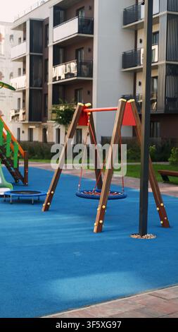 Modern urban children's playground with blue safety floor and residential buildings in the background Stock Photo