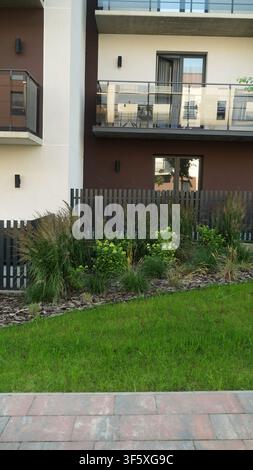 Modern apartment building exterior with balconies, lush green landscaping, and grass lawn in front Stock Photo