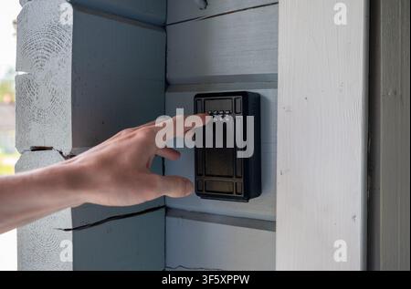Person entering access code on secure outdoor key lock box mounted on wooden house wall for safe property access Stock Photo