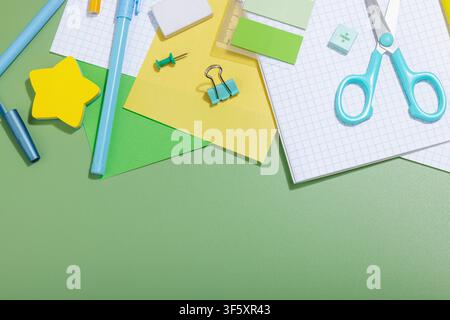 Back-to-school concept, flat lay composition of school supplies on a green background. Notebooks, pens, pencils, scissors, sticky notes, and stationer Stock Photo