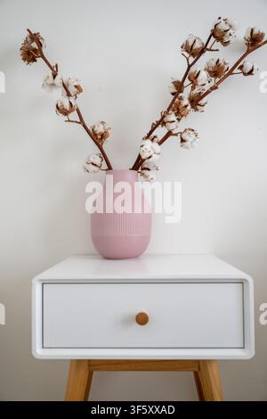 Minimalist pink vase with natural cotton branches on white bedside table in modern Scandinavian interior Stock Photo