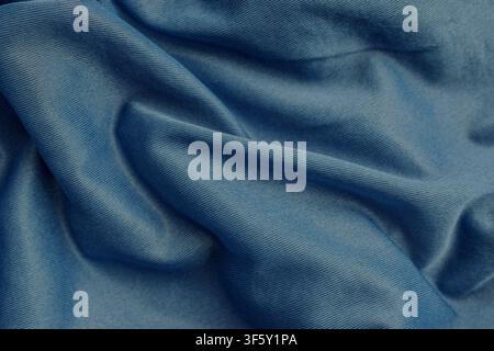 Draped dark blue denim style knitted cotton fabric background with diagonal ribbed texture and wave folds for autumn fashion apparel and sewing concep Stock Photo