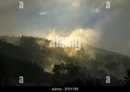 Sunbeams through the grey clouds and fog in the mountains of Galdames on a rainy winter day Stock Photo