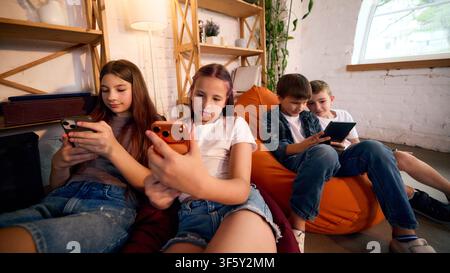 Group of children using smartphones and tablets while relaxing together Stock Photo