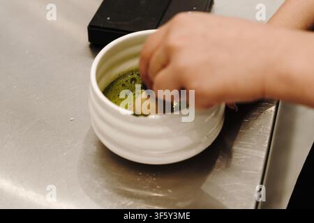 Bamboo whisk mixing matcha tea inside a ceramic bowl to create a smooth texture and foam. Traditional Japanese tea preparation in close-up. Stock Photo