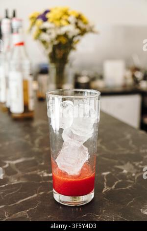 Ice cubes added over fresh strawberry puree inside a serving glass before assembling an iced layered beverage. Refreshing drink preparation in close Stock Photo