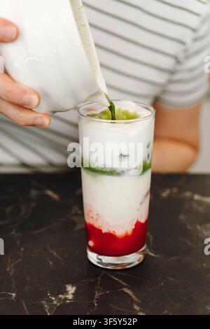 Freshly prepared matcha poured over cold milk to create vibrant green layers in an iced latte. Modern cafe beverage assembled by hand. Stock Photo