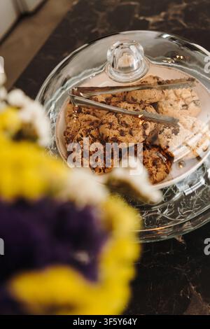 Fresh chocolate chip cookies displayed under a glass dome with serving tongs in a modern cafe. Homemade pastries presented for customers. Stock Photo